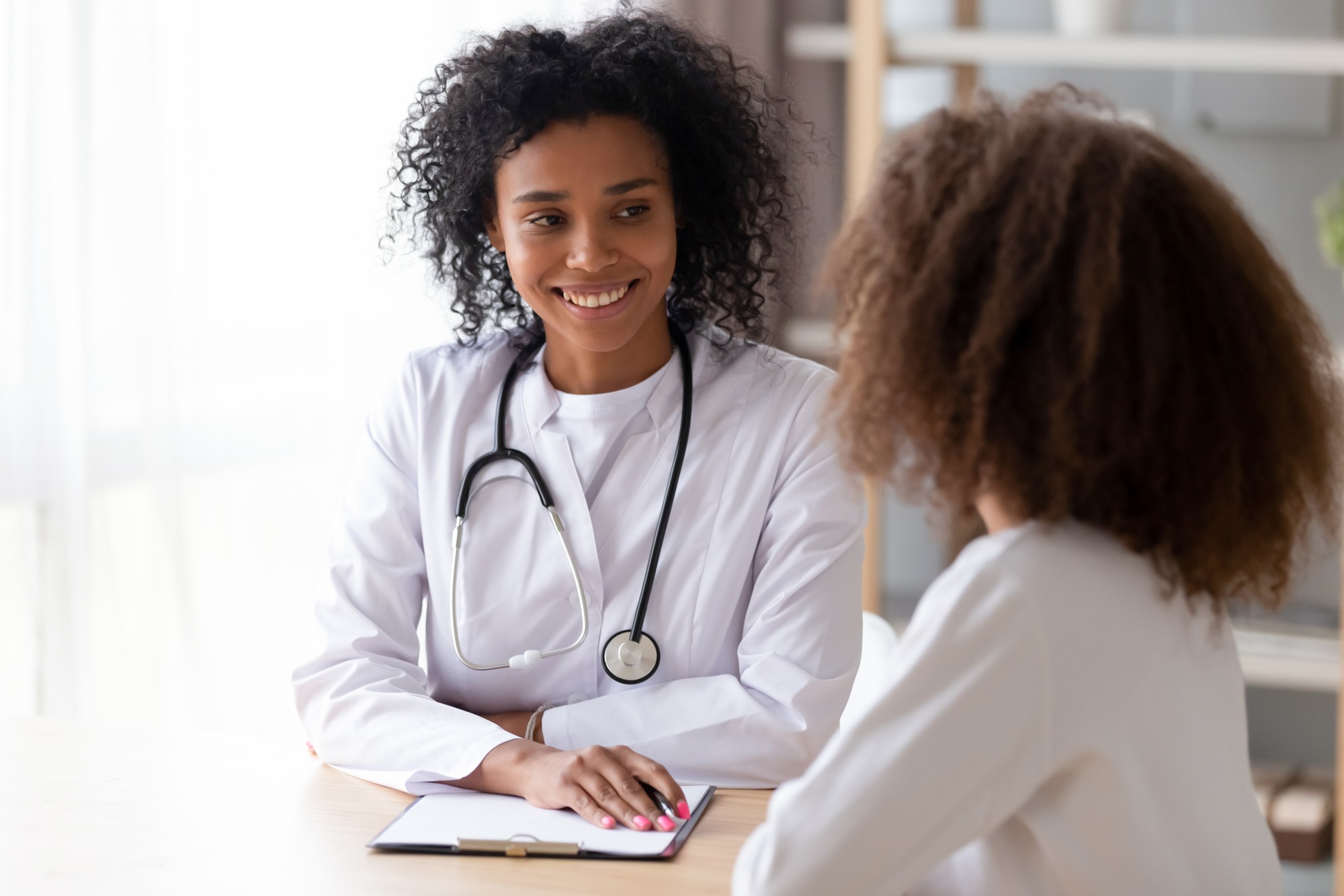 American doctor psychotherapist, therapist counsellor or pediatrist in white coat listens teen girl during reception at clinic.