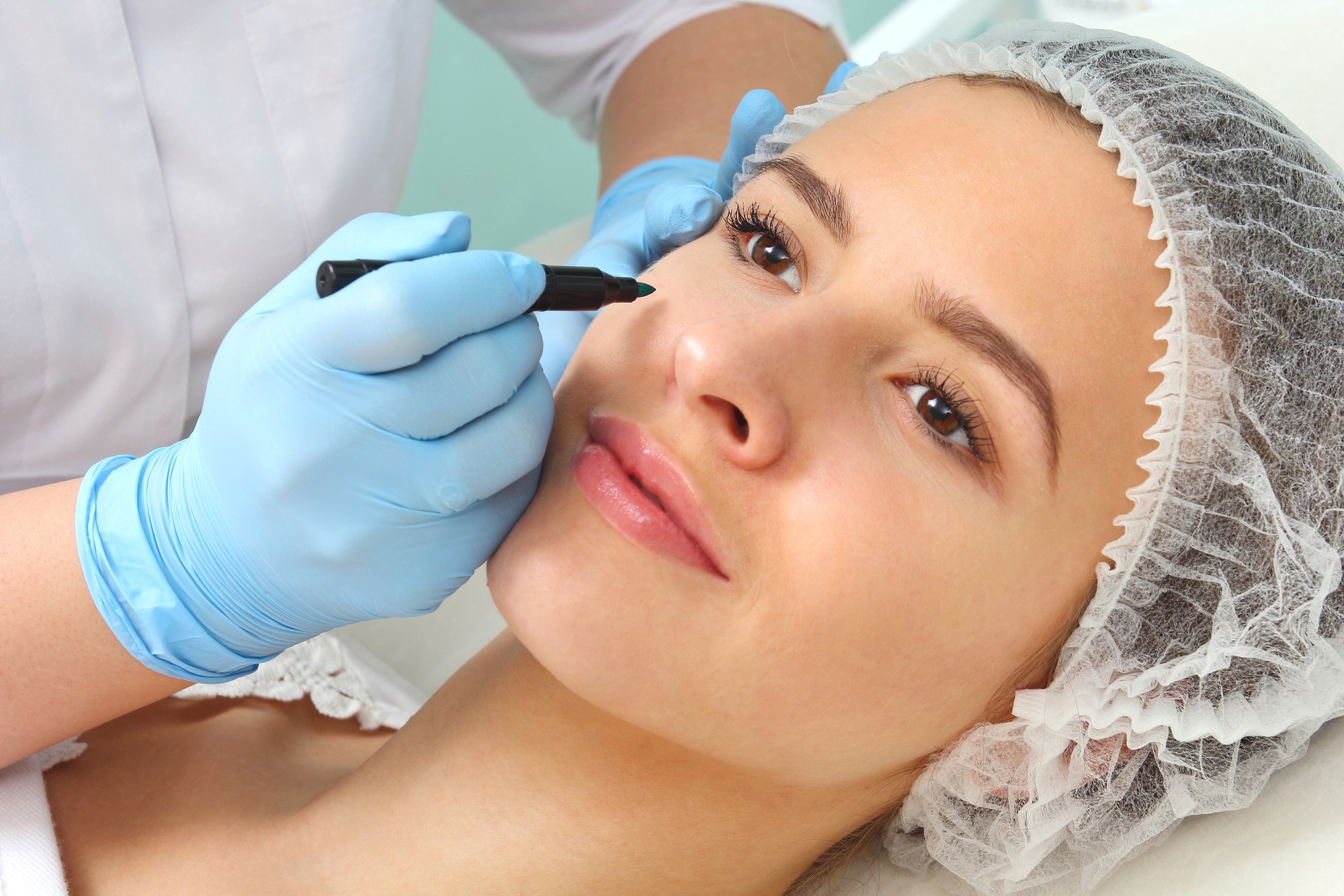 Plastic surgeon drawing lines over eyelid of a nice young female before cosmetic operation