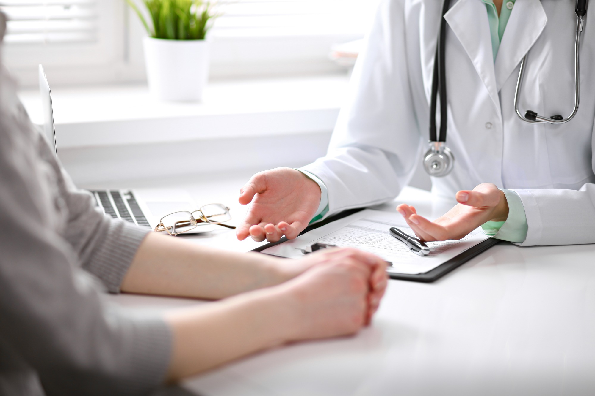 Close up of doctor and patient sitting at the desk near the window in hospital