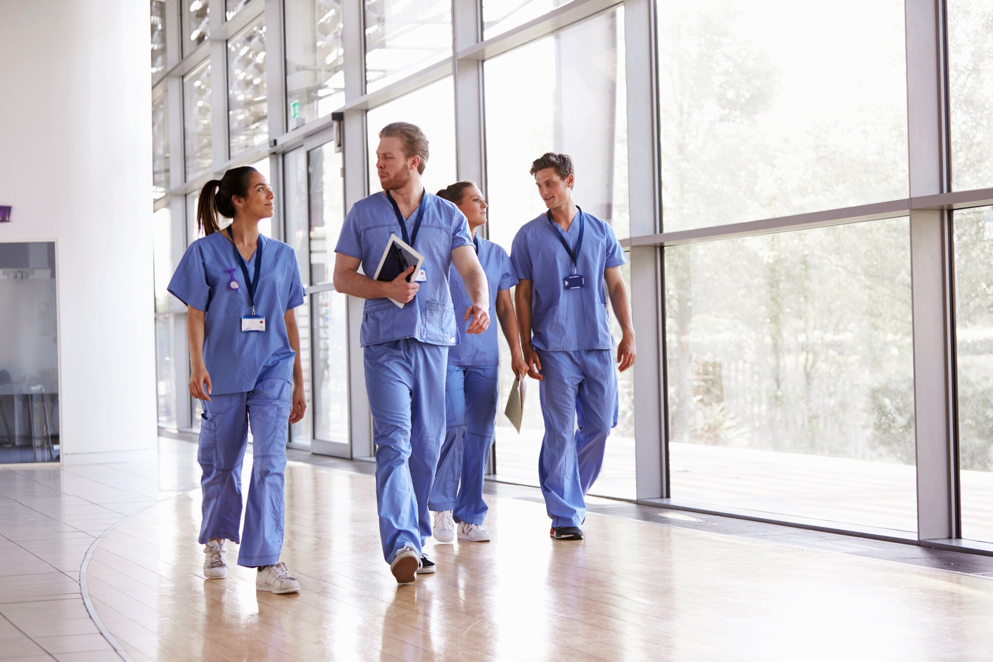 Four healthcare workers in scrubs walking in corridor